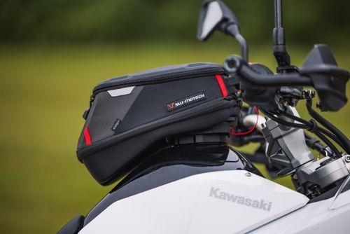 Black tank bag with red accents mounted on a white Kawasaki motorcycle's handlebars.
