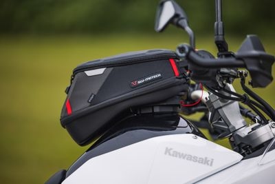 Black tank bag with red accents mounted on a white Kawasaki motorcycle's handlebars.
